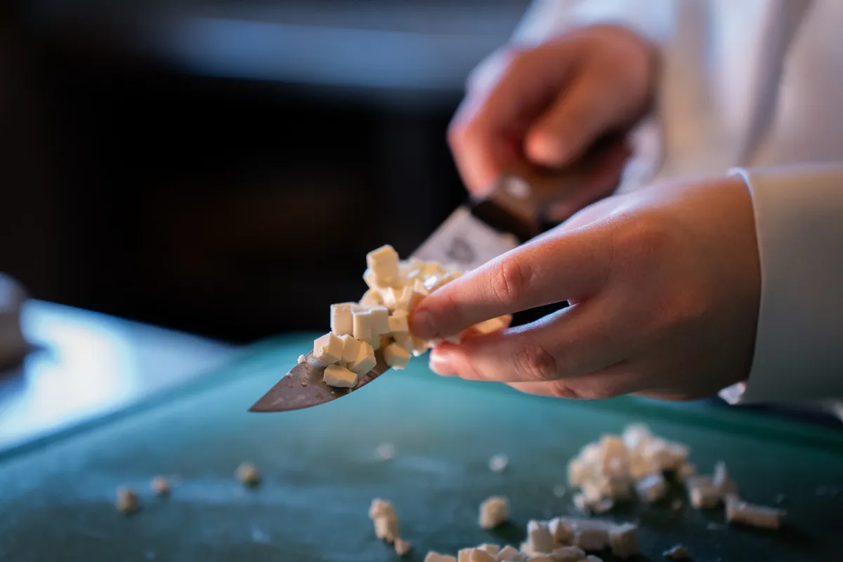 Hände schneiden Feta auf dem Schneidebrett in feine Würfel