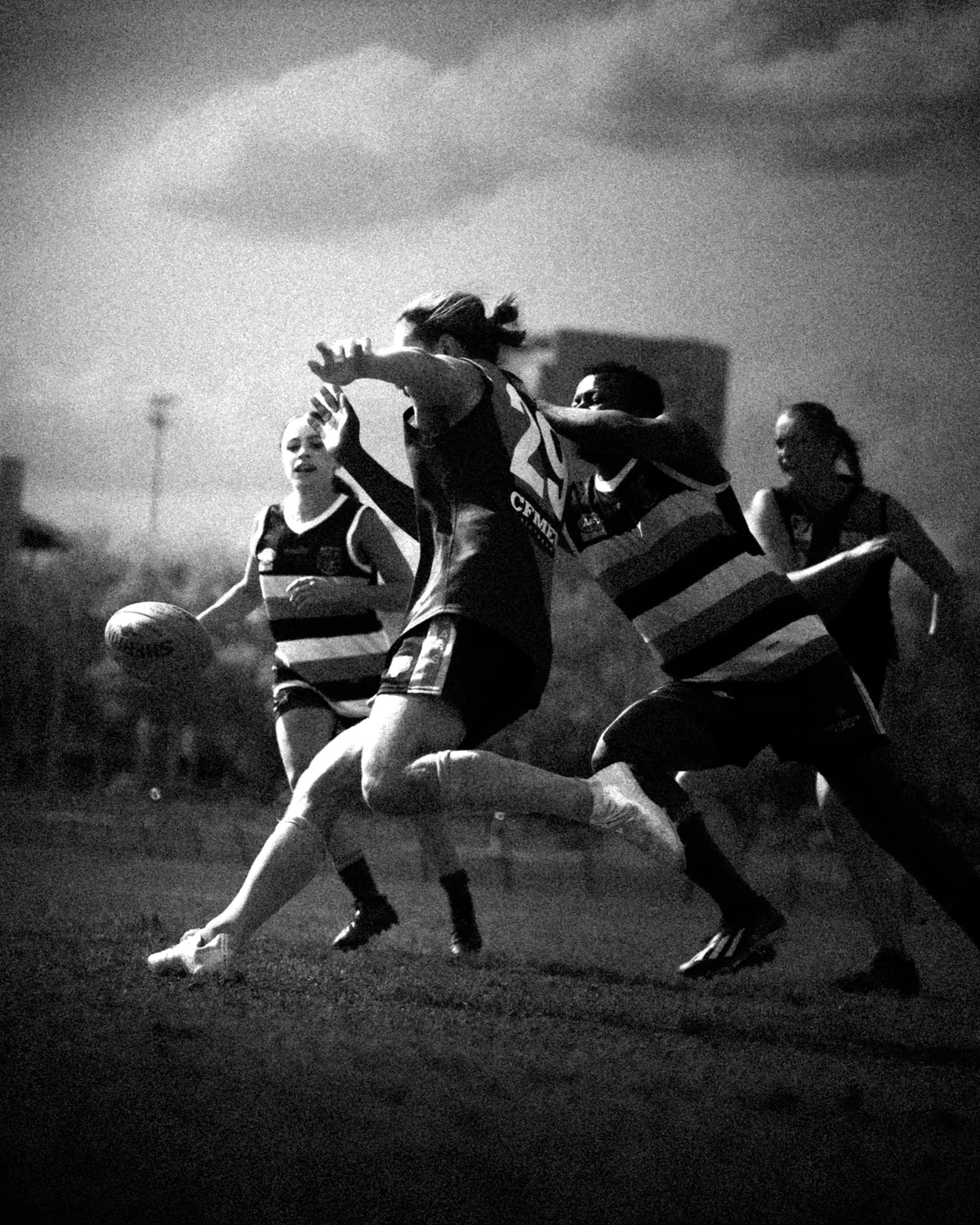 Schwarzweiss: Eine Spielerin kickt den Ball, bedrängt von zwei Gegenspielerinnen im Streifentrikot