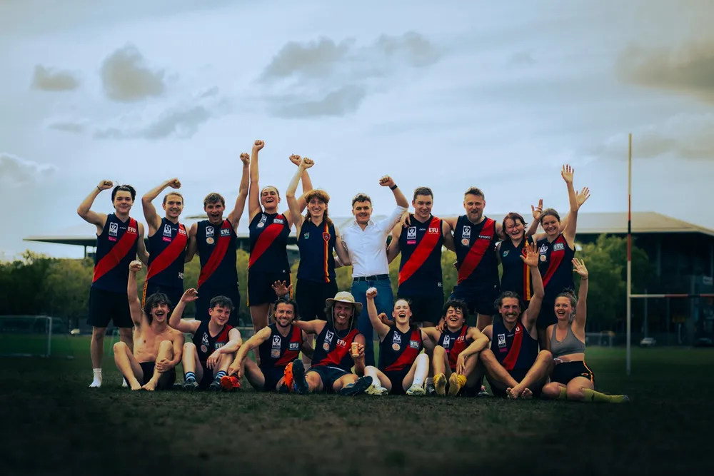 Jubelndes Teamfoto nach dem Spieltag: Spielerinnen und Spieler recken die Arme in den Abendhimmel