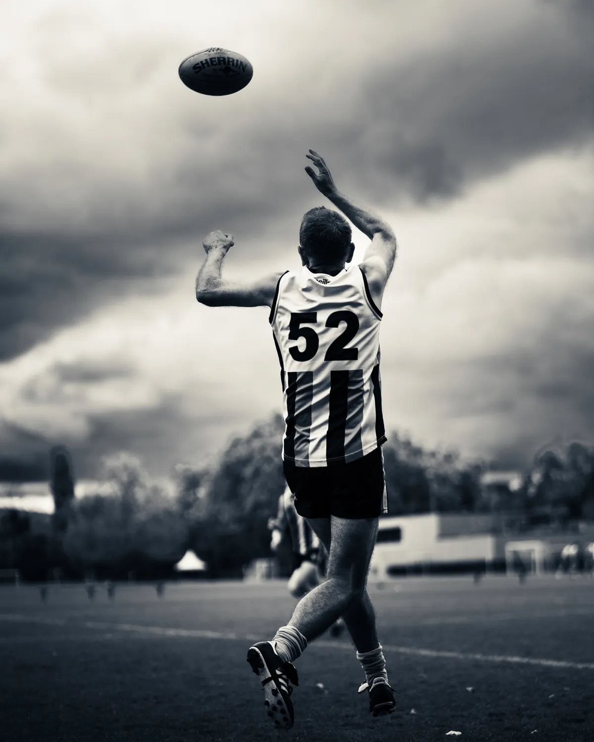 Schwarzweiss: Spieler mit der Nummer 52 streckt sich nach dem hoch fliegenden Ball, dahinter eine dramatische Wolkendecke