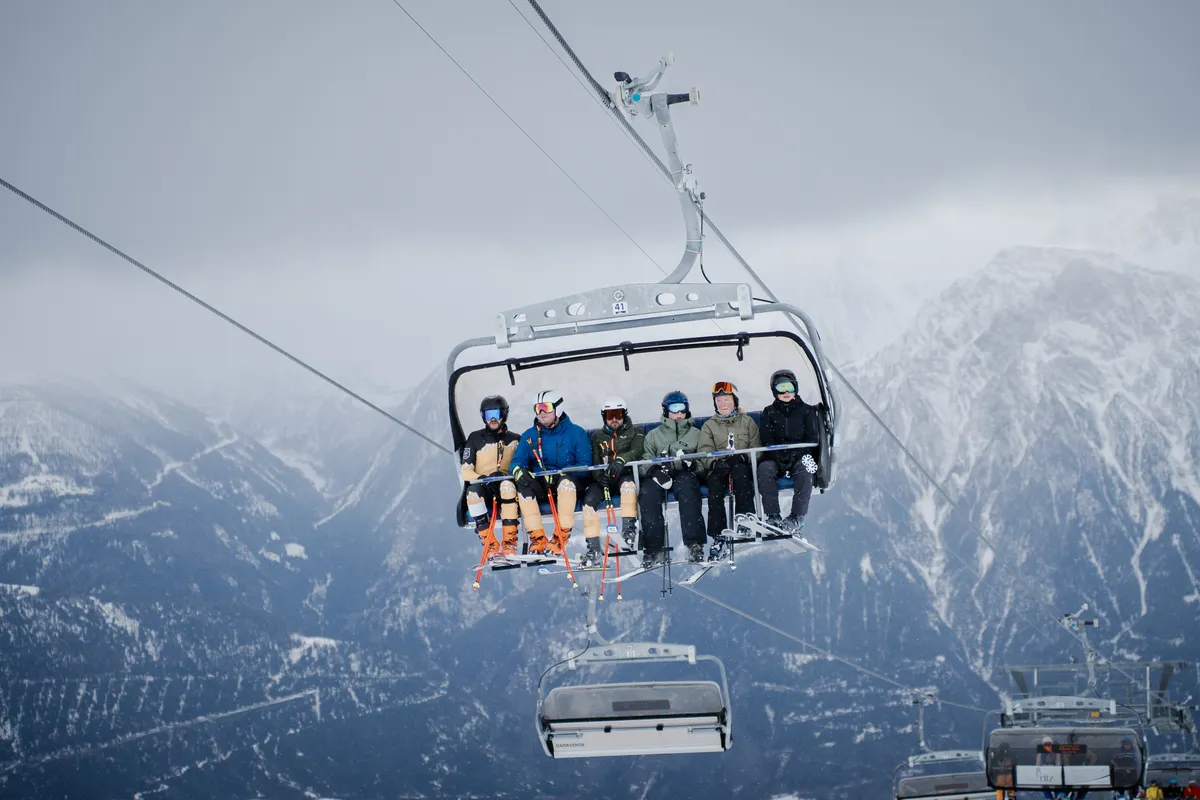 Sessellift mit sechs Skifahrenden vor nebligem Bergpanorama