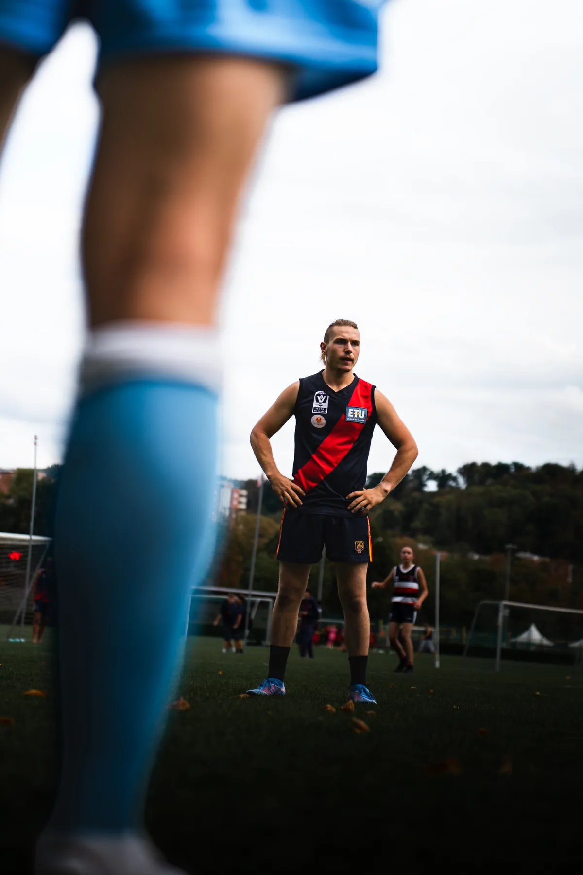 Durch die Beine eines Mitspielers hindurch fotografiert: ein Spieler der Bern Bears steht mit den Händen in den Hüften auf dem Feld