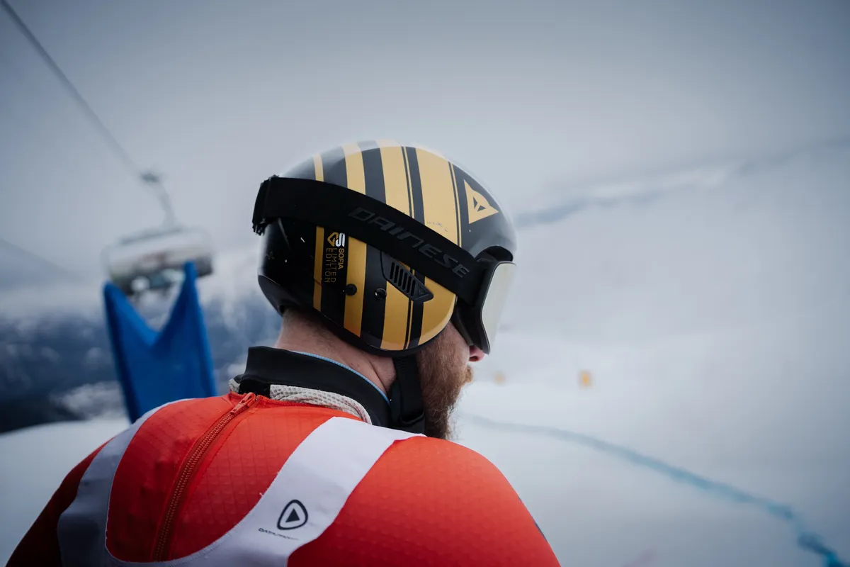 Rennläufer mit goldenem Helm blickt von der Kante die Piste hinab