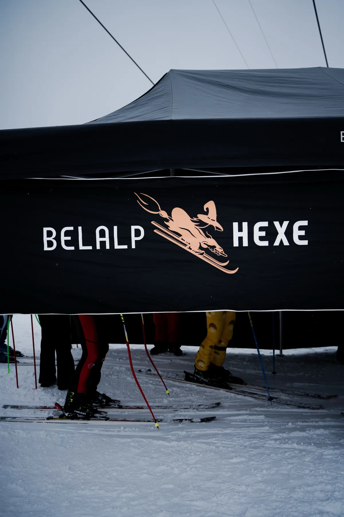 Zelt mit dem Logo der Belalp Hexe, davor Ski und kostümierte Beine