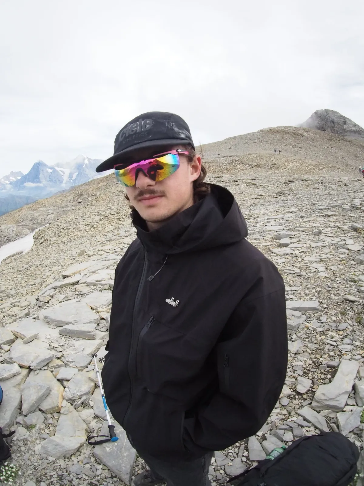 Maël mit bunter Sportbrille auf einem Berggipfel, hinten Schneeberge