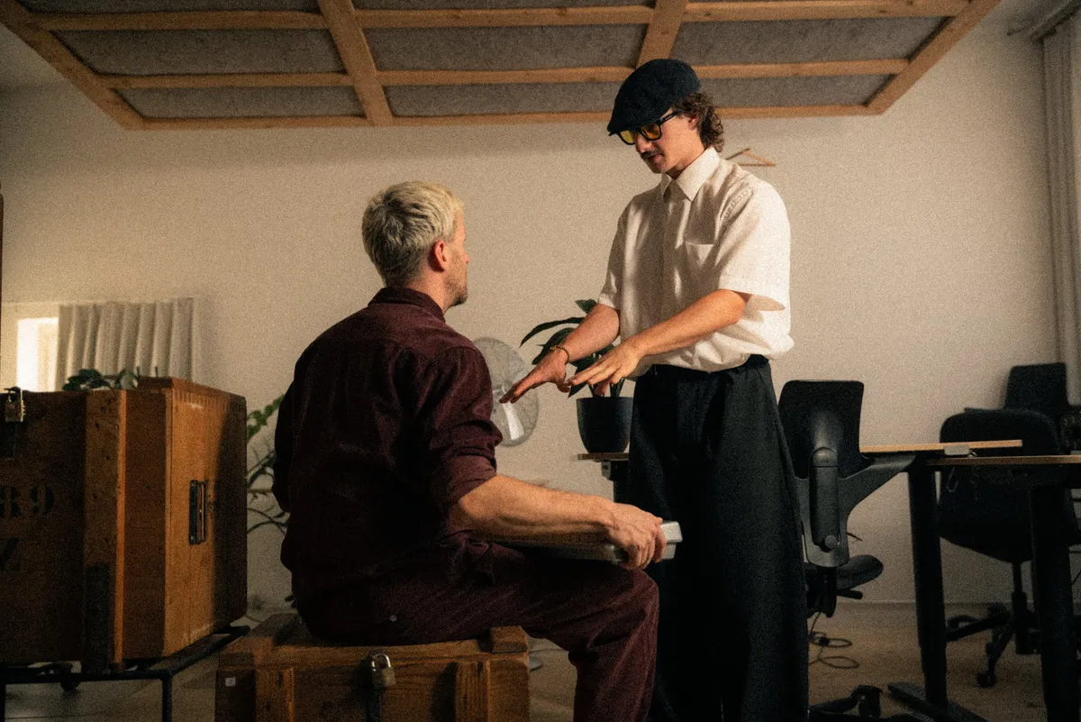 Maël im Gespräch mit einem sitzenden Mann in einem Raum voller Holz