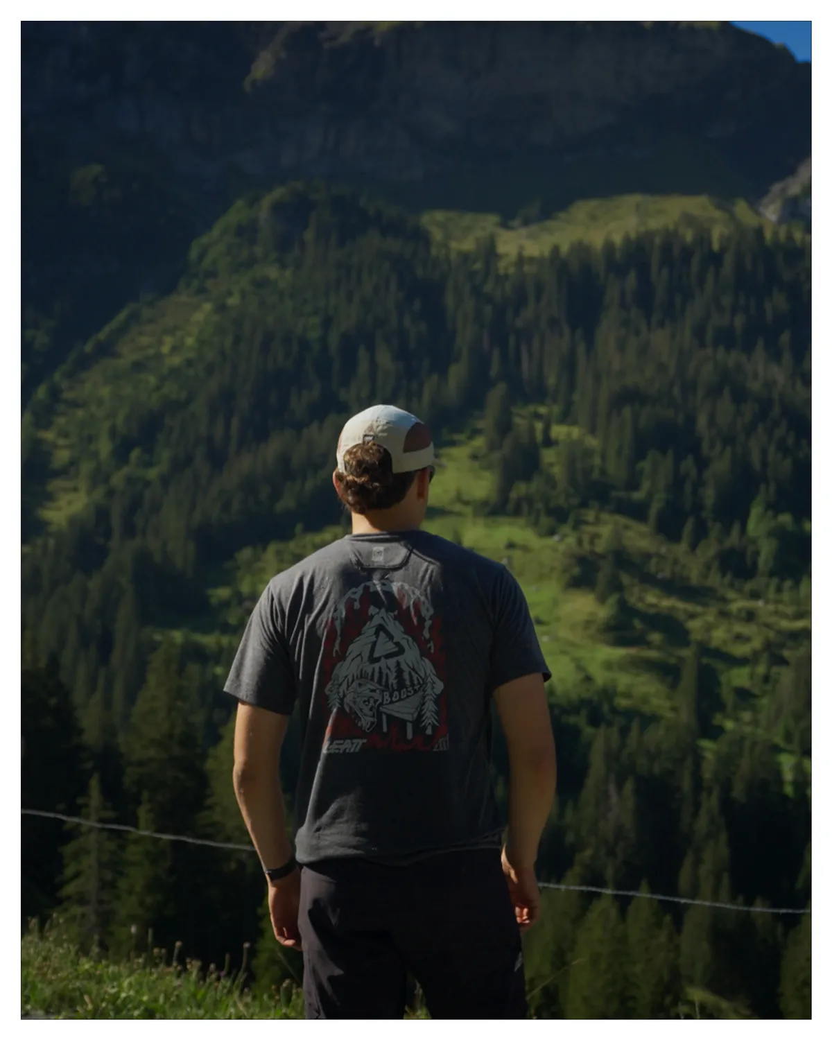 Wanderer mit Cap blickt über das bewaldete Tal, Bild mit weissem Rand